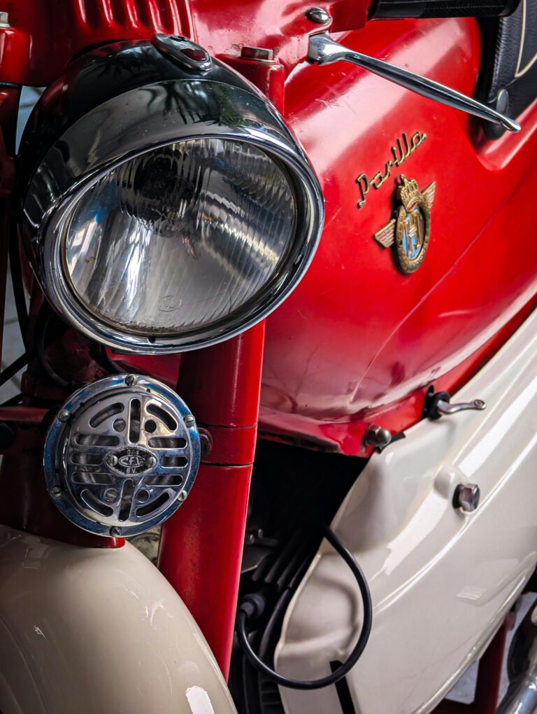 Detailed view of a vintage red motorcycle showing headlight and emblem.
